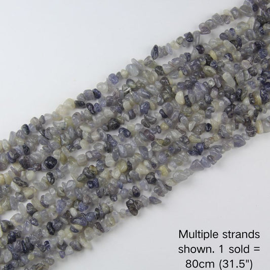 Multiple strands of natural 5-8mm Iolite chip beads laid out flat, showing the variety of colors and textures in bulk inventory