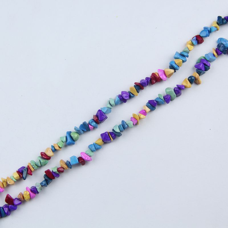 Single irregular colorful howlite bead necklace laid flat on light surface, 31-inch rainbow strand with natural black matrix on each bead