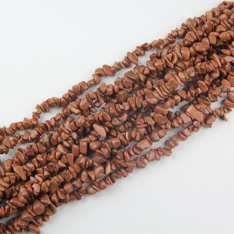 Multiple gold sandstone long necklaces stacked together, showing rich amber-brown color and copper glitter sparkles across all strands