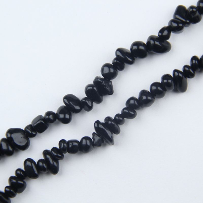 closeup of irregular black obsidian beads lined up on white background showing 5 to 8mm size variation
