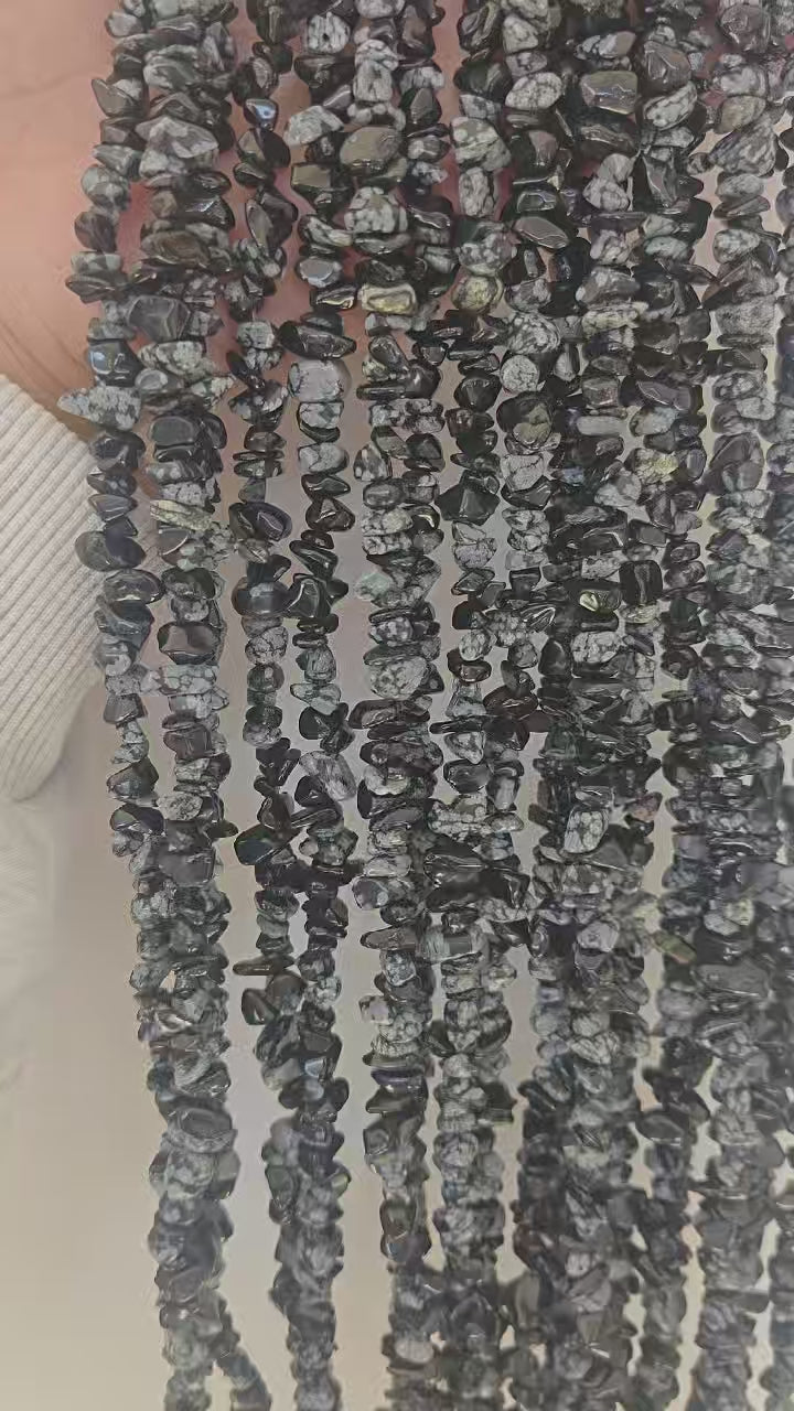 slow motion closeup of snowflake obsidian beads showing unique white snowflake patterns on black stone