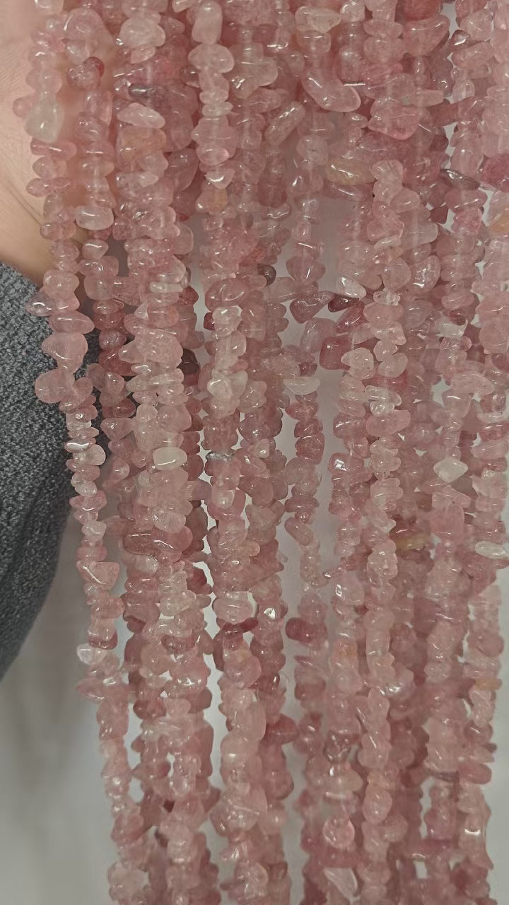 Video showing multiple strands of natural red strawberry quartz beads, each 31.5 inches long, featuring 5-8mm irregular round beads threaded on durable nylon cord. Strands are displayed hanging to showcase sweet pinkish-red color, sparkly inclusions, and natural variations.
