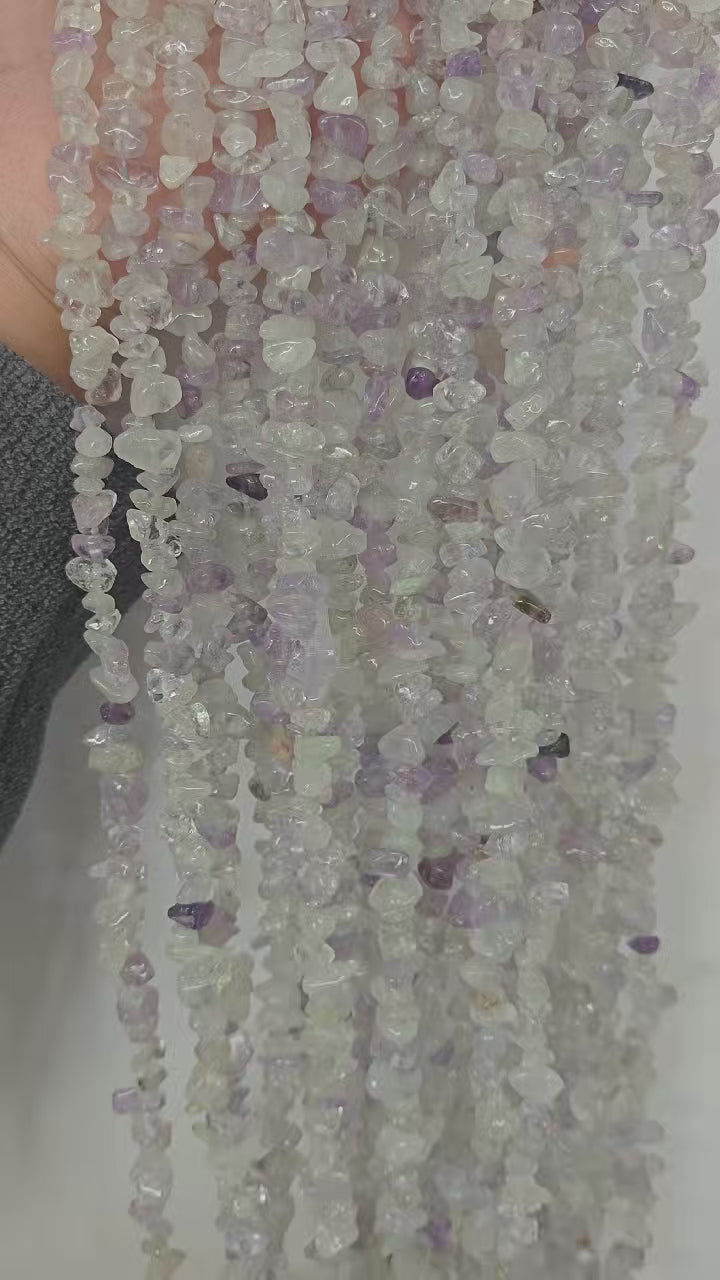 Video showing multiple strands of natural purple-white crystal beads, each 31.5 inches long, featuring 5-8mm irregular round beads threaded on durable nylon cord. Strands are displayed hanging to showcase soft lavender and white color variation.