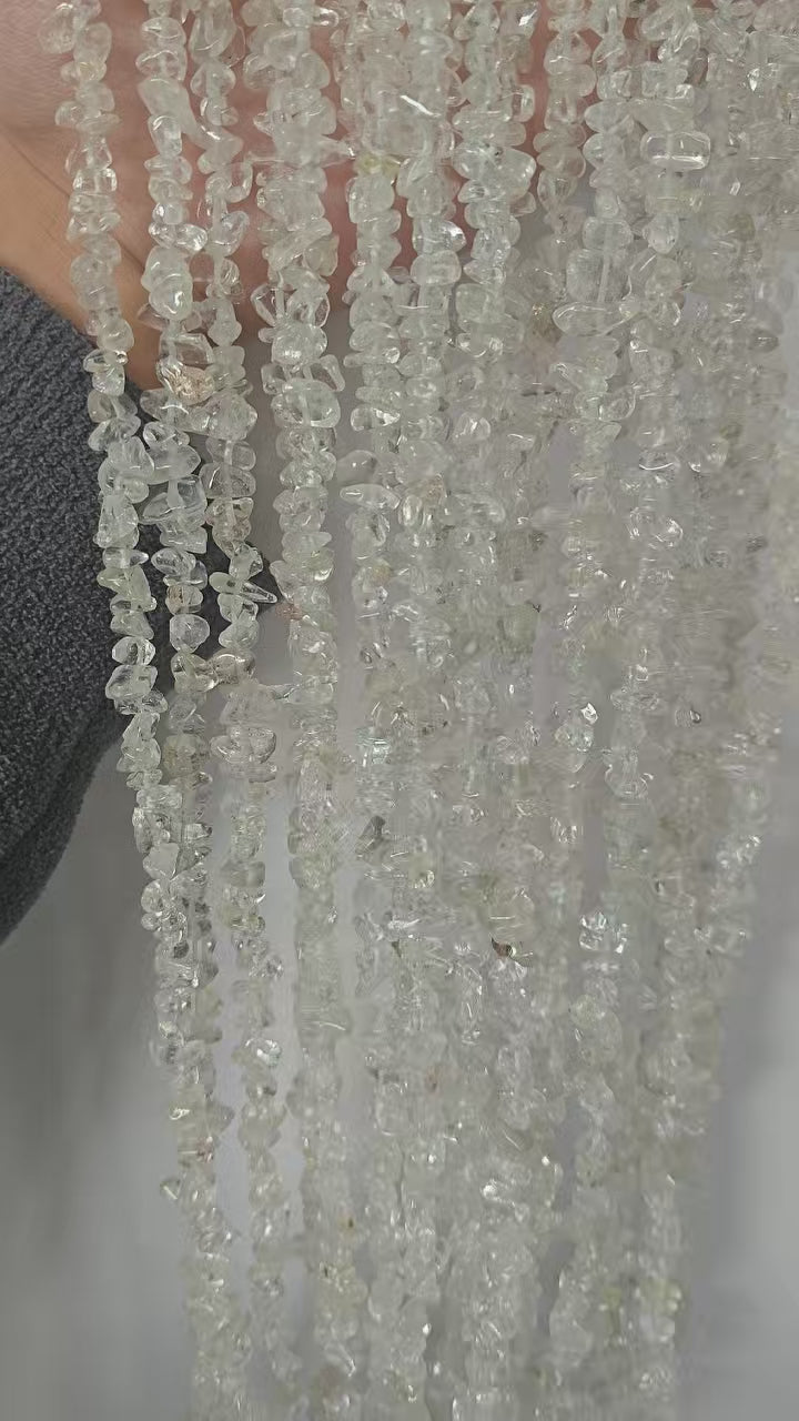 Video showing multiple strands of natural clear quartz beads, each 31.5 inches long, featuring 5-8mm irregular round beads threaded on durable nylon cord. Strands are displayed hanging to showcase transparency, light refraction, and length.