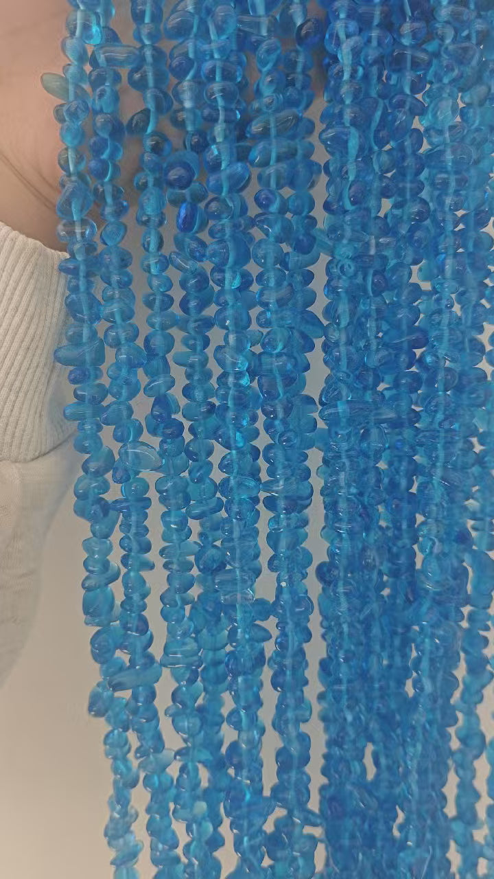 Showcase of natural blue glass irregular round beaded necklace. Displays the 31.5-inch length, 5-8mm bead size and translucent texture of the cool blue glass jewelry. 