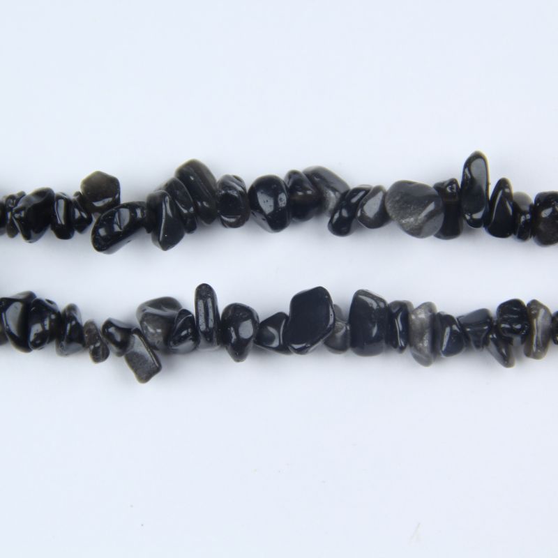 closeup of silver obsidian beads catching direct light revealing metallic silver shimmer and rainbow-like reflections on black stone