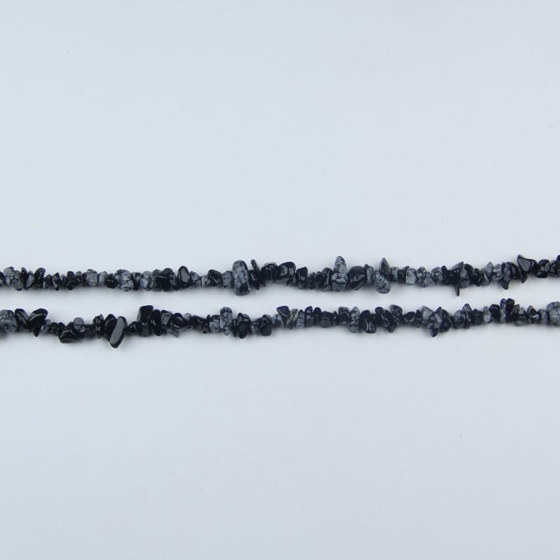 single snowflake obsidian long bead necklace laid flat on white background showing white snowflake patterns on black stone
